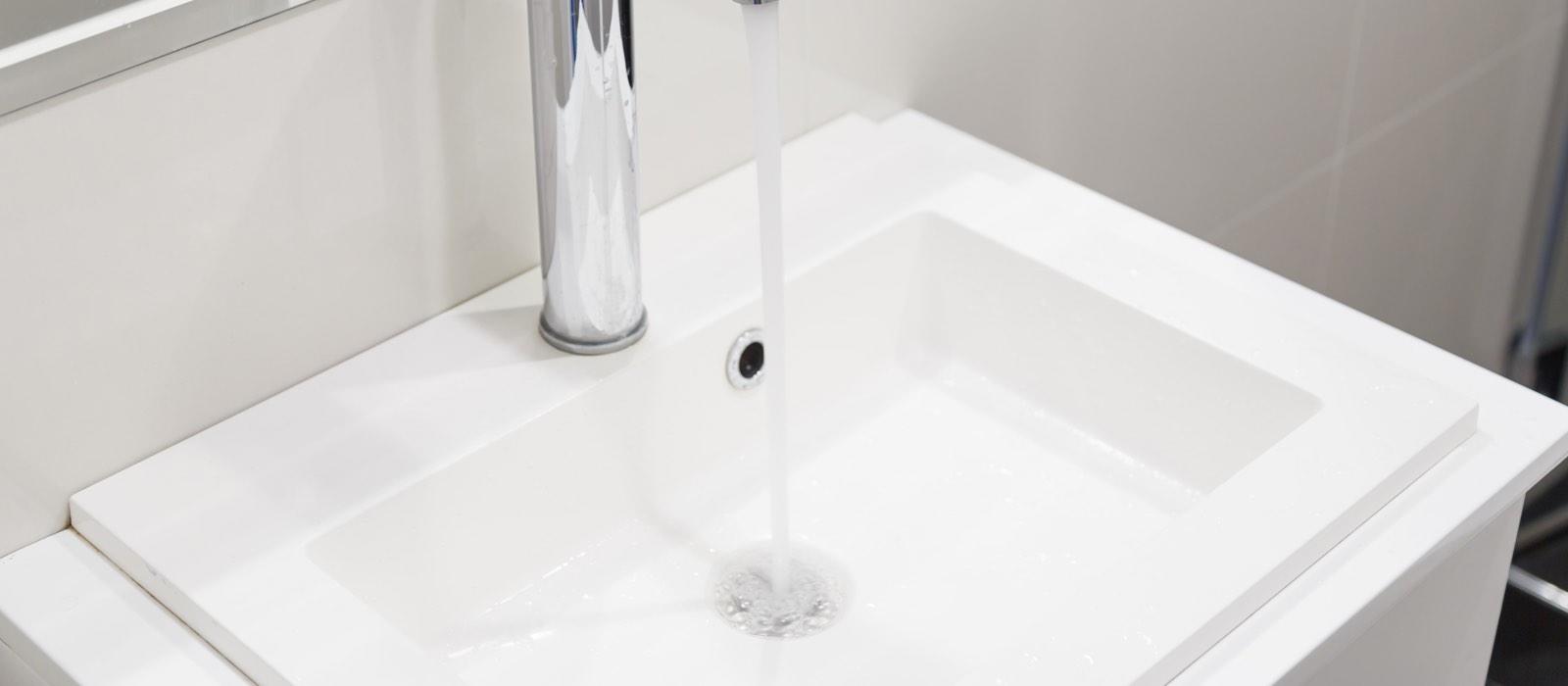 Silver faucet pouring water into rectangular white sink